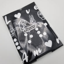 Load image into Gallery viewer, The tee inside a plastic bag. A Disability Creations logo sticker on top of the plastic bag.