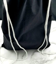 Load image into Gallery viewer, The back of the drawstring bag. The bag is black with white string handles.