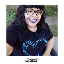 Load image into Gallery viewer, A selfie of Nelly wearing the community Love t-shirt. Her wheelchair is visible in the photo.
