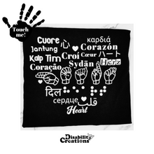 Load image into Gallery viewer, A black t-shirt that says "Heart" in nineteen languages shaping a heart. The languages used in the tee are English, Spanish, American Sign Language, Braille, Italian, Chinese, Indonesian, Greek, Turkish, Irish, French, Japanese, Portuguese, Finnish, German, Hindi, Russian, Arabic, and Vietnamese. Raised vinyl used to be able to read "heart" in Braille.