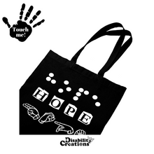 Load image into Gallery viewer, A Black tote bag that says &quot;Hope&quot; in three different languages in white vinyl. The first line is &quot;Hope&quot; in Braille. The second line has &quot;Hope&quot; in English, and the third line has Hope in American Sign Language- fingerspelling.
