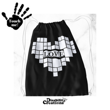Load image into Gallery viewer, A black drawstring bag with a white heart. In the middle of the heart, it says, "Love." Surrounding "Love" are small and large squares forming a heart. Raised vinyl is used to feel the design and read "Love."