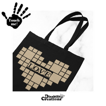 Load image into Gallery viewer, A Black tote bag with a camel heart. In the middle of the heart, it says, "Love." Surrounding Love are small and large squares forming a heart. Raised vinyl is used to read "Love."