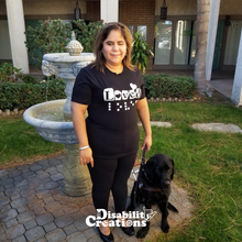 Load image into Gallery viewer, Juanita is standing with her service animal in front of a fountain. She is wearing the Loved (Braille Accessible) T-Shirt!