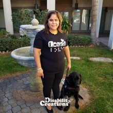 Load image into Gallery viewer, Juanita is standing with her service animal in front of a fountain. She is wearing the Loved (Braille Accessible) T-Shirt!
