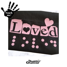 Load image into Gallery viewer, A folded black shirt with the pink design. On the top left is a black hand. On the palm, it says, "Touch me." The Disability Creations logo is at the bottom.