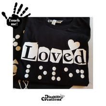 Load image into Gallery viewer, The Loved Shirt, Black shirt with white design. Behind the shirt is the Hope in 3 Languages shirt. On the top left is a black hand. On the palm, it says, &quot;Touch me.&quot; The Disability Creations logo is at the bottom.
