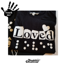 Load image into Gallery viewer, The Loved Shirt, Black shirt with white design. Behind the shirt is the Hope in 3 Languages shirt. On the top left is a black hand. On the palm, it says, "Touch me." The Disability Creations logo is at the bottom.