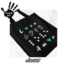 Load image into Gallery viewer, A black tote bag. The first line is love in English. The letter "O" is replaced by a purple heart. The second line has "love" in American Sign Language-fingerspelling. The third line has love in Braille. Finally, the four-line has love in Spanish - Amor. The letter "O" is replaced by a heart. The design is white except for the hearts, different colored hearts are available. 