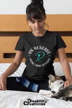 Load image into Gallery viewer, A woman sitting on her bed petting her cat. She is wearing the On Reserve Using Mini-Spoons Shirt. The post says New Disability Shirt., Mint. July 28. www.DisabilityCreations.com