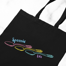 Load image into Gallery viewer, A Black tote bag with an outline of three engraved vintage spoons (pink, yellow, and turquoise) lined up side to side with the handles on the right. It says, "Spoonie life." "Spoonie" is located above the first spoon. "Life" is below the third spoon's handle.