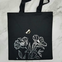 Load image into Gallery viewer, Tote bag that has a small gold butterfly is flying over silver line detail flowers.