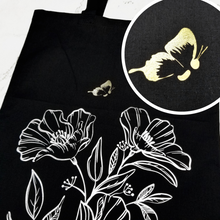Load image into Gallery viewer, A Black double-sided tote bag. On one side, a small gold butterfly is flying over silver line detail flowers. The butterfly&#39;s body is a semicolon. On the other side, &quot;Believe&quot; in silver handwringing with a semicolon replacing the &quot;I.&quot; 
