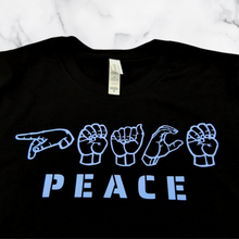 Load image into Gallery viewer, The Peace in ASL T-Shirt folded on top of a white marble table.