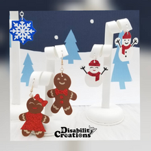 Load image into Gallery viewer, Mrs. &amp;Mr. Snowie Earrings and the Gingerbread Couple Earrings hanging on earring stands with a Winter Wonderland background.
