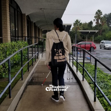Load image into Gallery viewer, Danyelle walking up an accessible ramp using her white cane. She is wearing the Dots are my Thing #Braille Drawstring Bag.
