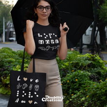 Load image into Gallery viewer, A woman is wearing a black shirt, the Hope in 3 languages tee with nude trousers holding an opened umbrella. She has the &quot;Love in 4 Languages&quot; with the red hearts tote bag.
