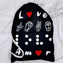 Load image into Gallery viewer, The backpack says &quot;Love&quot; in four different languages. The first line is love in English. The letter &quot;O&quot; is replaced by a red heart. The second line has love in American Sign Language- fingerspelling. The third line has love in Braille. Finally, the four-line has love in Spanish - Amor. The letter &quot;O&quot; is replaced by a red heart. It has drawstring handles.
