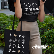Load image into Gallery viewer, A woman is wearing a black shirt, the Hope in 3 languages tee with nude trousers holding an opened umbrella. She has the &quot;Love in 4 Languages&quot; with the nude  hearts tote bag.

