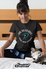 Load image into Gallery viewer, A woman sitting on her bed petting her cat. She is wearing the On Reserve Using Mini-Spoons Shirt. The post says New Disability Shirt.,  Mint. July 28. www.DisabilityCreations.com
