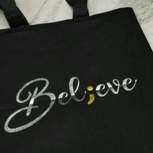 Load image into Gallery viewer, A tote bag that has &quot;Believe&quot; in silver handwringing with a semicolon replacing the &quot;I.&quot; 
