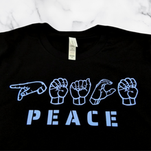 Load image into Gallery viewer, The Peace in ASL T-Shirt folded on top of a white marble table.

