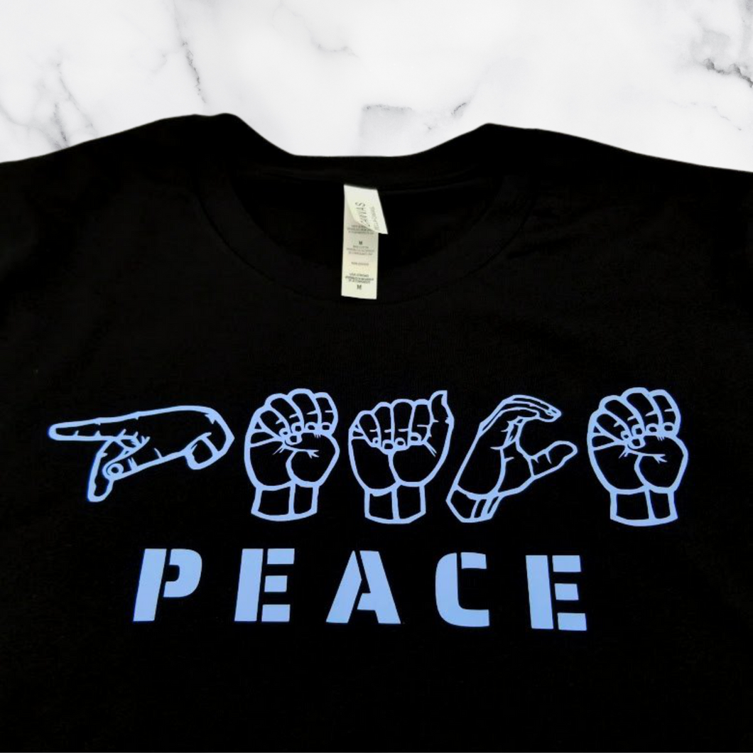 The Peace in ASL T-Shirt folded on top of a white marble table.